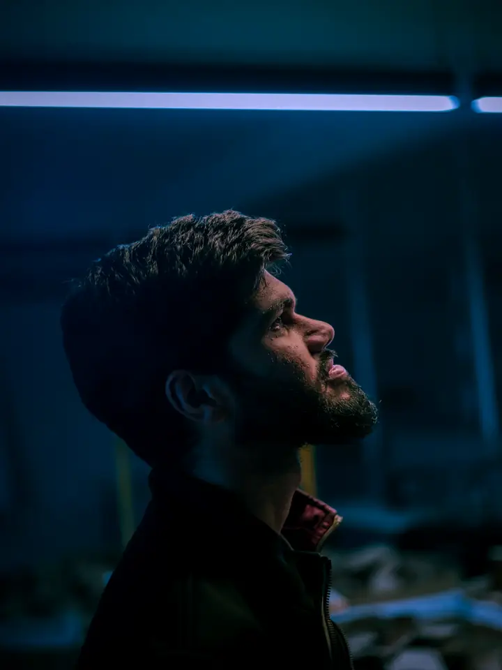 A man in profile in a dark room lit by blue light