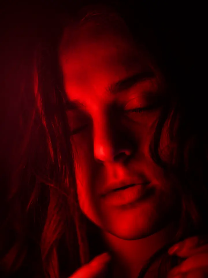 A woman with her face washed in red light, eyes half closed