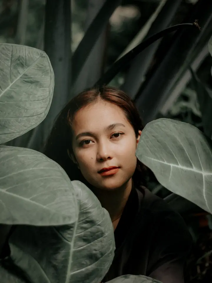 A woman sitting calmly among large green leaves