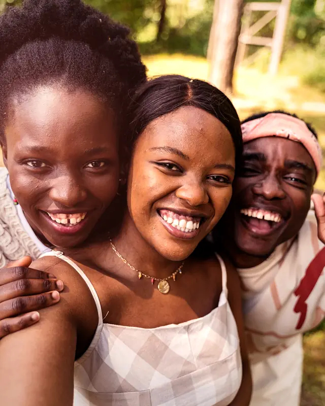 Three friends laughing together outdoors, cheek to cheek