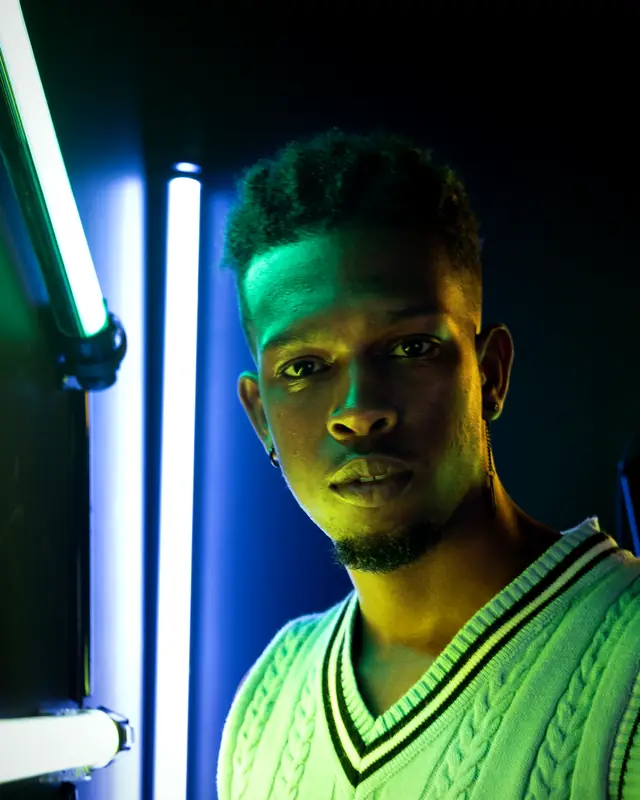A young man in a cricket sweater lit by green and blue neon tubes