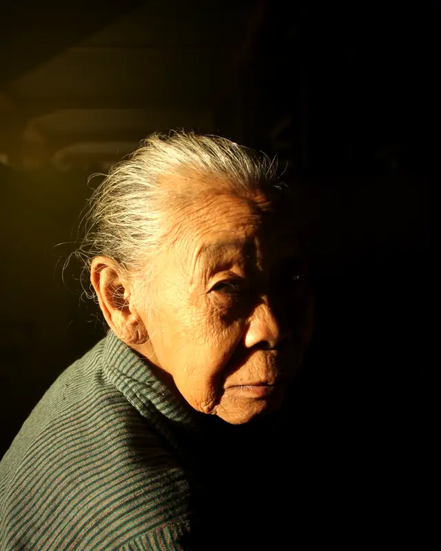 An older woman in warm late-afternoon light, eyes lowered