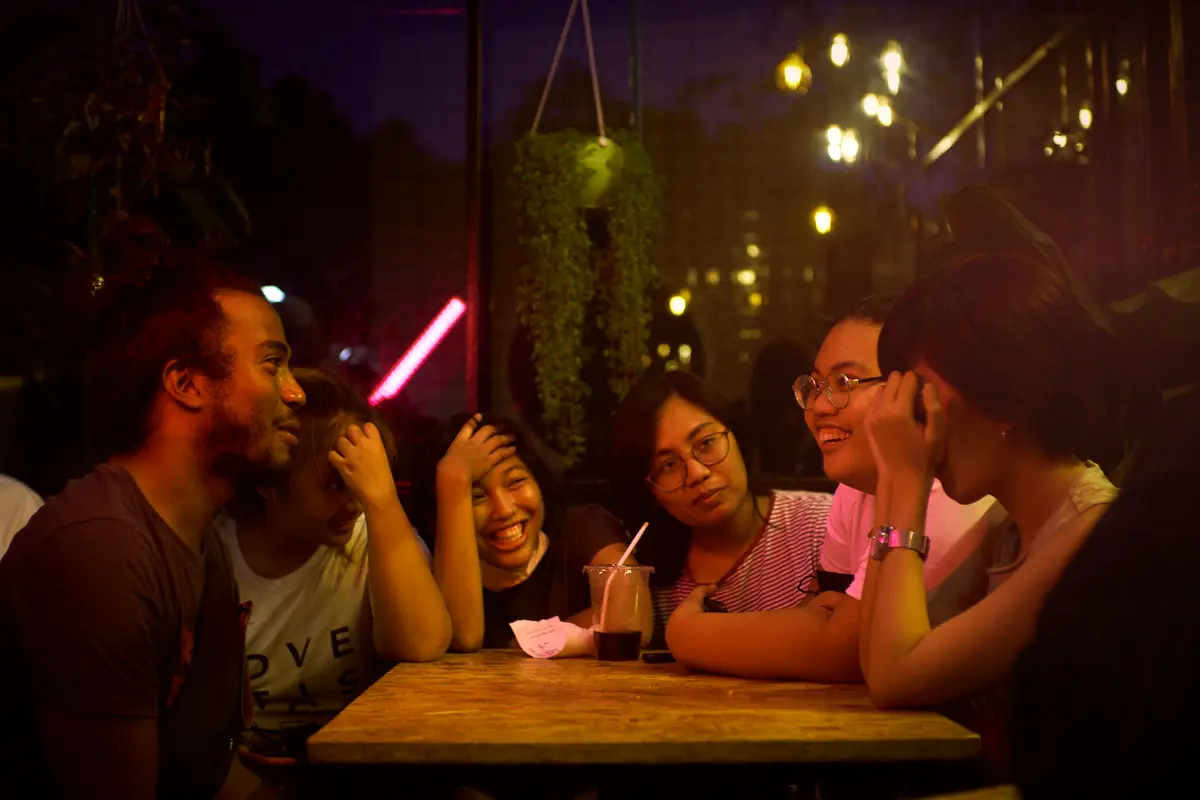 Friends laughing around a cafe table at night under string lights
